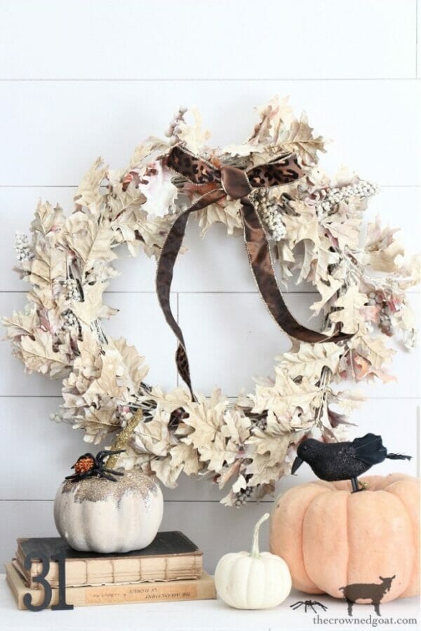 beige leaf wreath with brown velvet bow and pale pumpkins with black bird