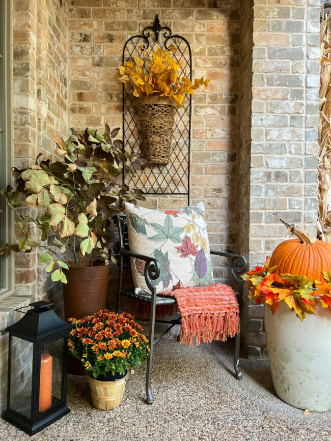 porch with fall pillow in chair, fall stems, mum and lantern