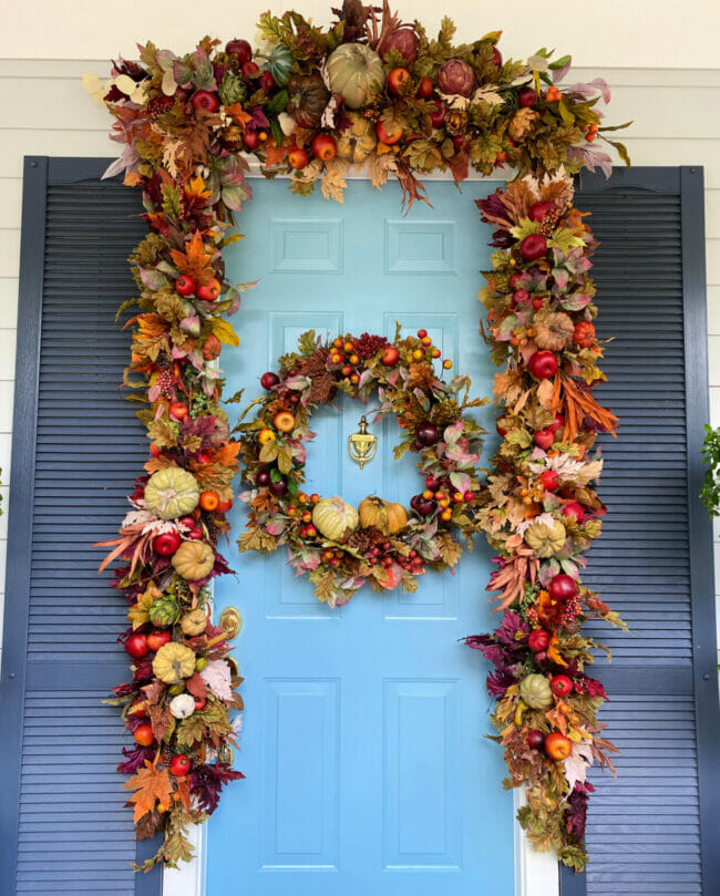 blue front door with fall garland around door and a wreath