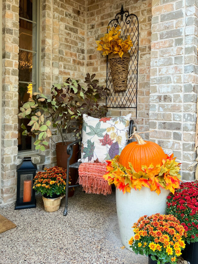 chair on porch with fall mums, lantern and pumpkin on planter