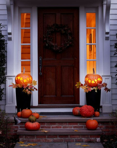 dark front door with 2 urns with lighted pumpkins on top