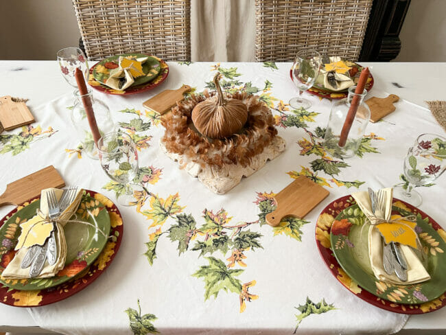 overhead shot of green and gold thanksgiving table with place settings and feather and pumpkin centerpiece