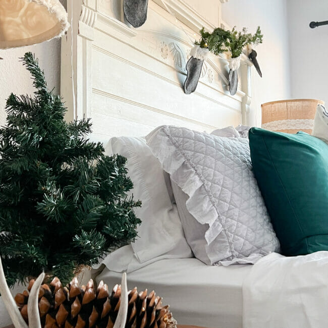 square print of bed with small Christmas tree on side table and mitten garland on headboard