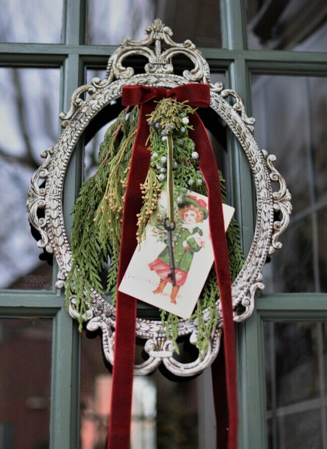 Oval frame with greenery, ribbon and vintage card on front door.
