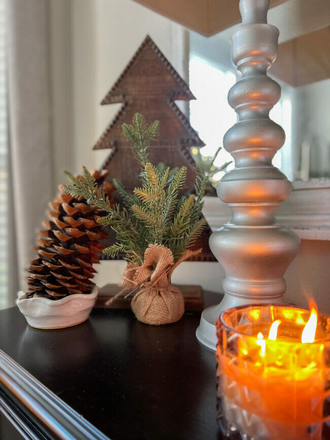 tall wooden tree, candle burning and a pinecone and small green tree with lamp