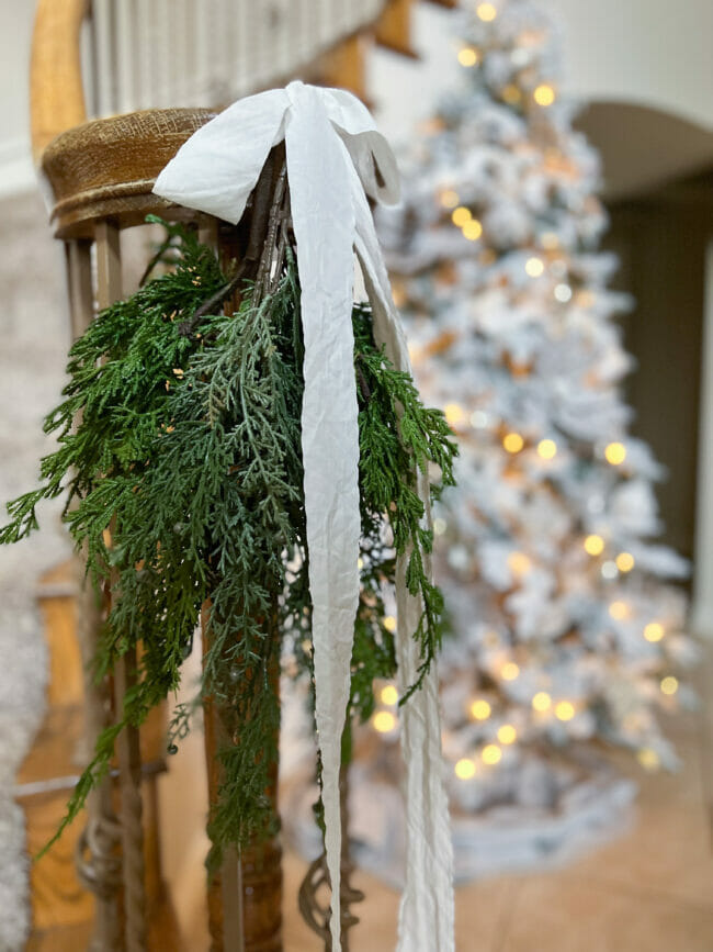 Faux greens with white bow hanging on stair railing