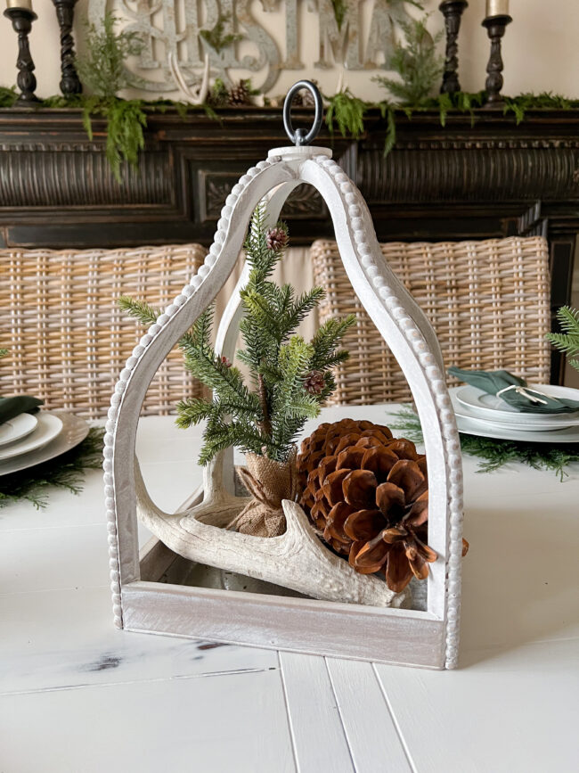 white lantern centerpiece with a small tree, antler and pinecone