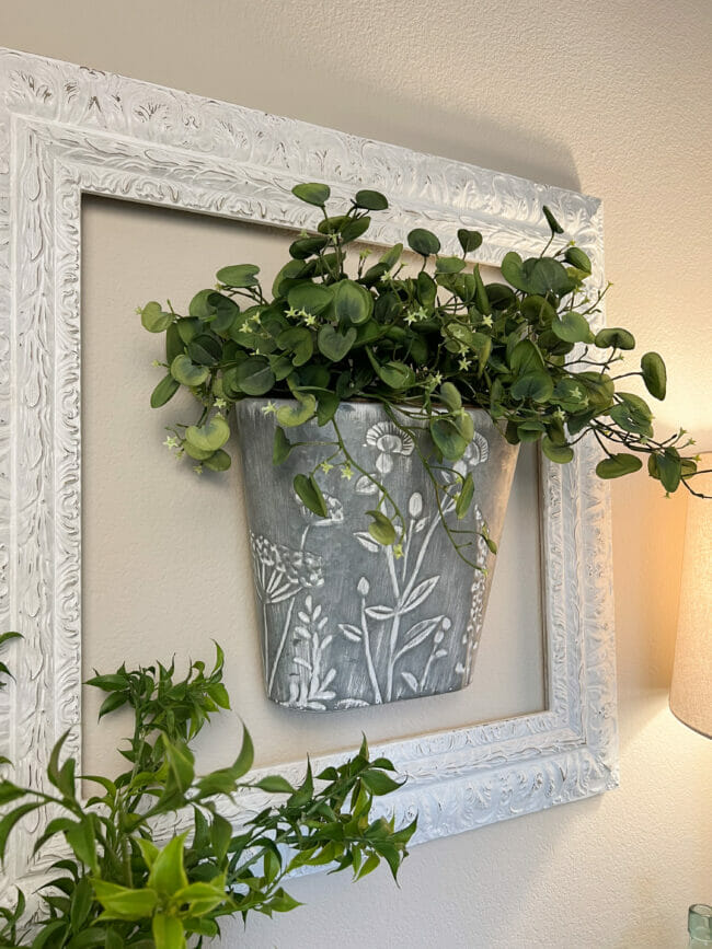 galvanized bucket with greenery hanging inside white frame on wall