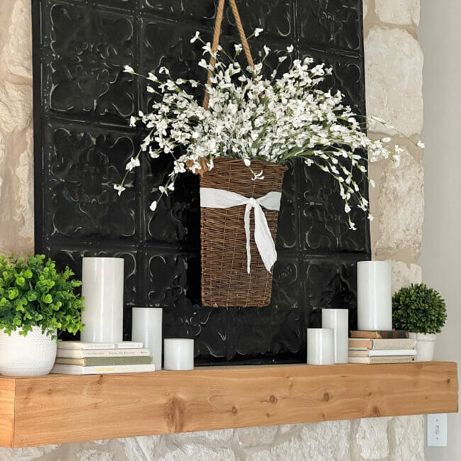 wood mantel with white candles, floral stems in hanging basket and books