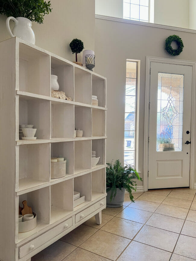 white cubby shelf with fern by front door