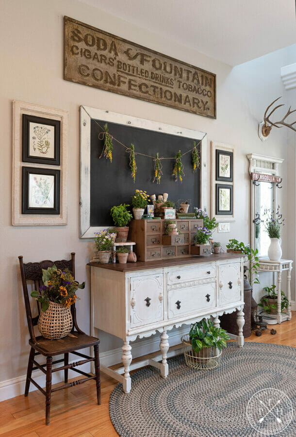 entry with chalkboard with hanging flowers and a sideboard with chest with plants inside drawers