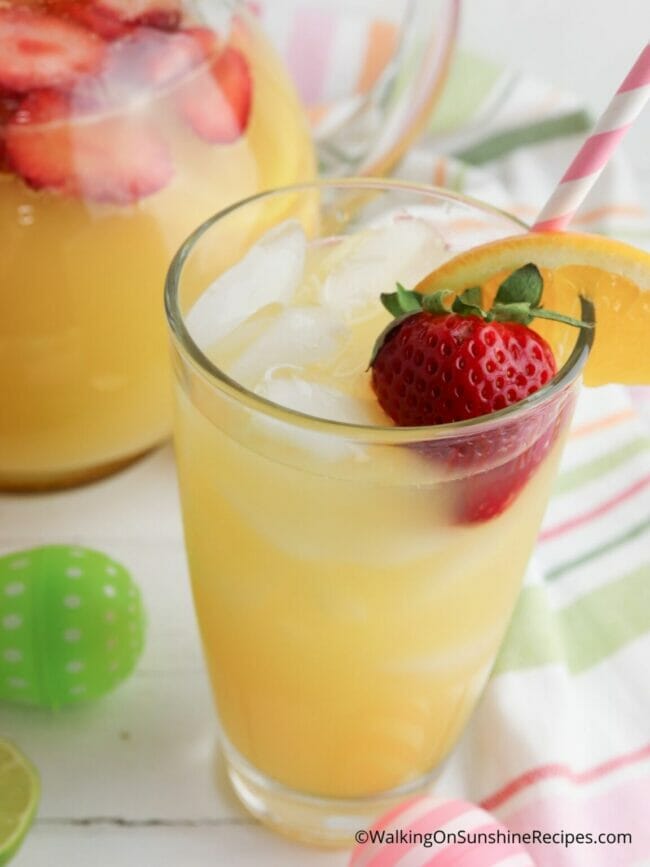 glass of orange colored punch with strawberry and straw