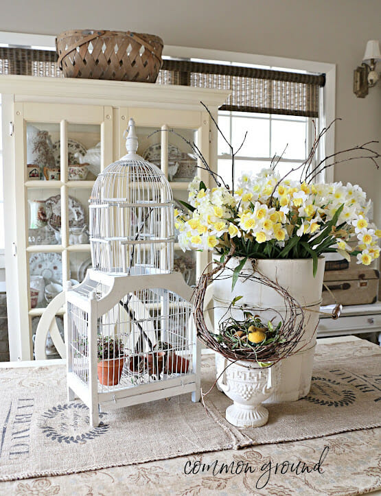 white birdcage, white bucket with yellow flowers and white urn with bird nest