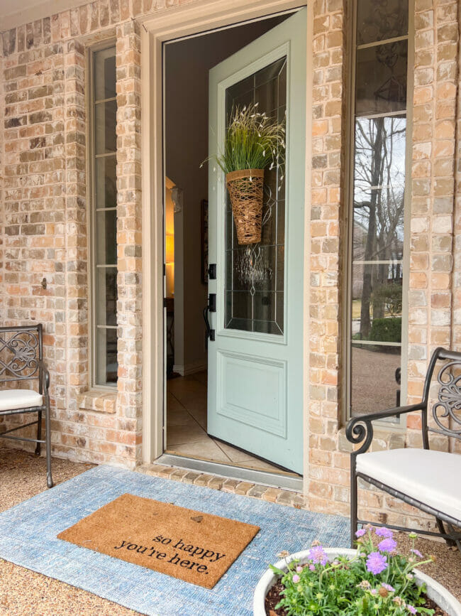 brick house with opened light mint colored door, blue rug and iron chairs