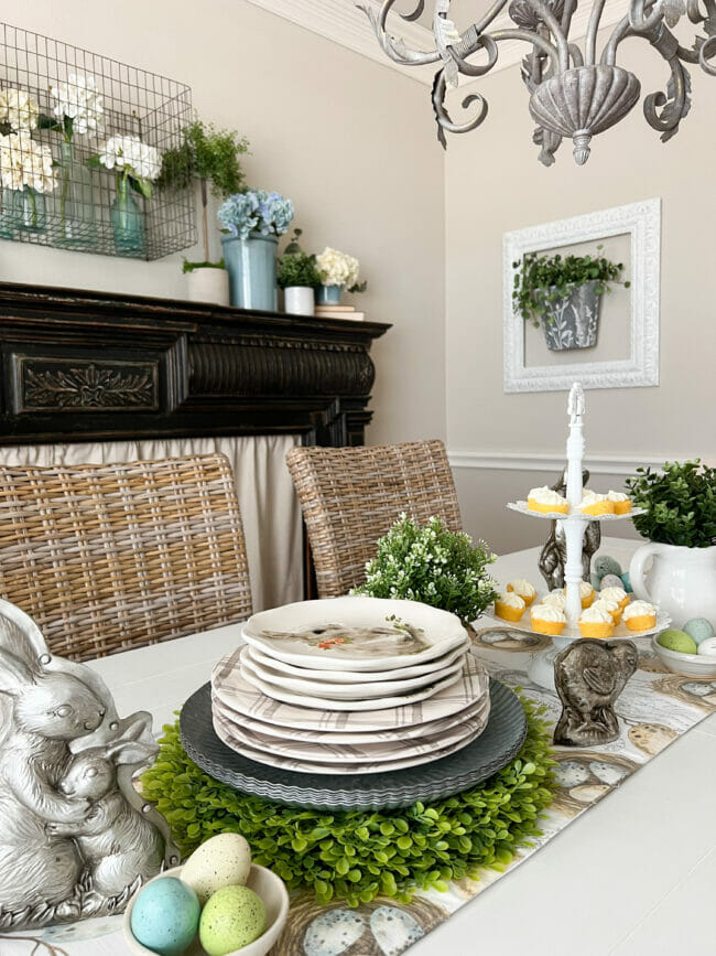 tablescape with silver bunnies, stsack of plates, greenery and tiered tray