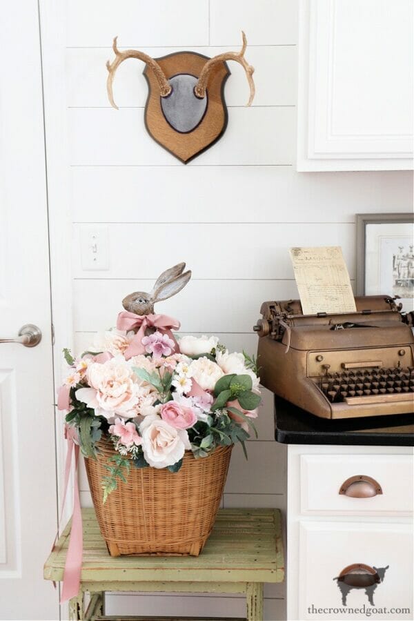 bunny in basket of flowers with antlers on the wall above it