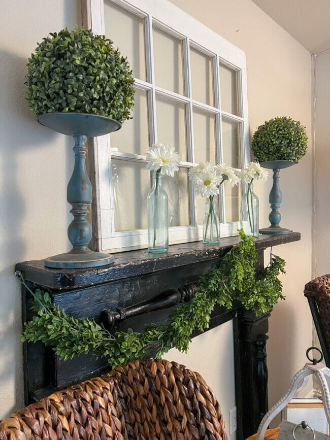 black mantel with boxwood garland, topiary balls and blue bottles with white daisies