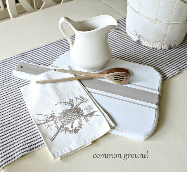 Striped breadboard with tea towel, small white pitcher and wooden spoons