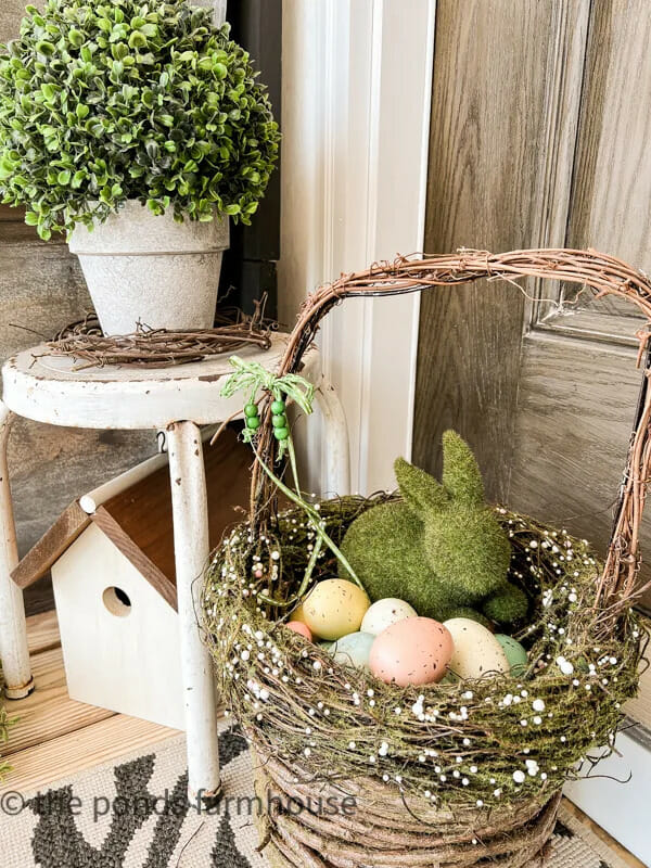 willow basket with moss bunny and eggs sitting by old white stool and birdhouse