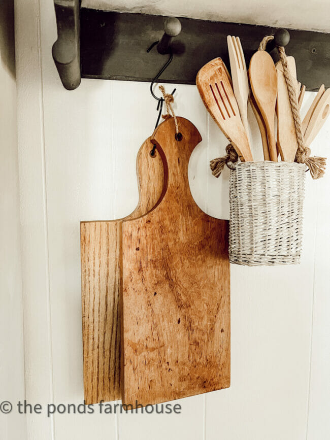 2 cutting boards haning with wooden spoons in white basket