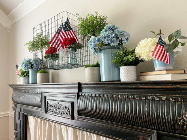 black mantel with patriotic decor, blue crocks with flowers and mini flags in bottles