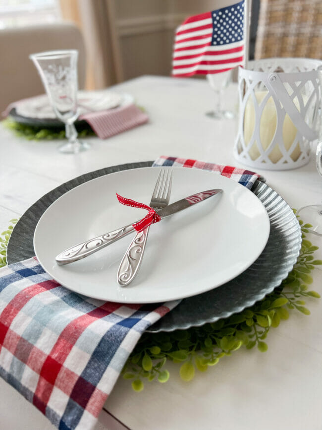 white place setting with patriotic decor on napkins and tied up silverware with mini flag in background