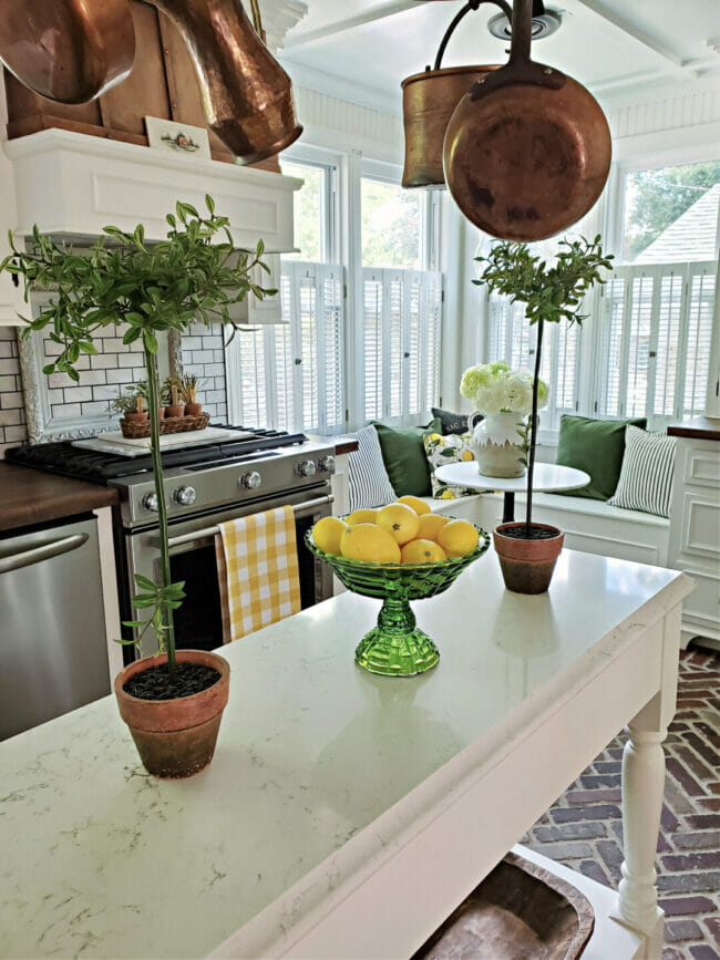 white kitchen island with green bowl of lemons and two topiaries