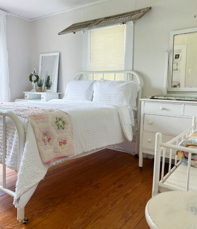 countryfied bedroom with bed, shutter over window, dresser and babybed