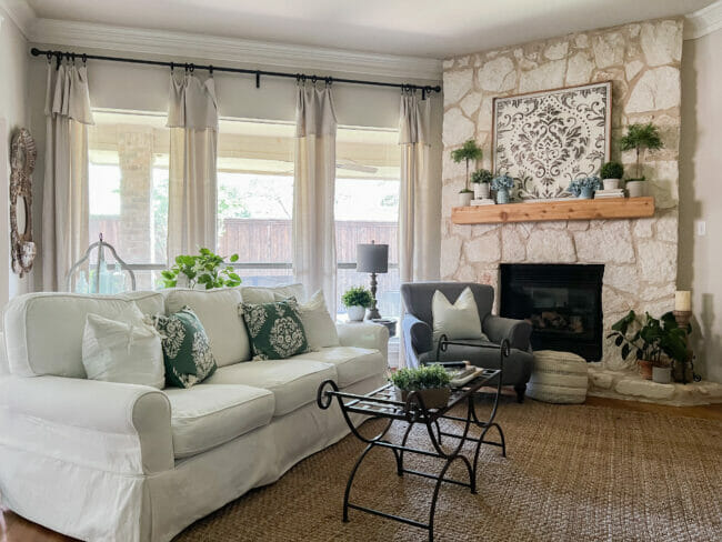 do what you want using a white sofa, stone mantel with topiaries and gray chair and green pillows in front of windows