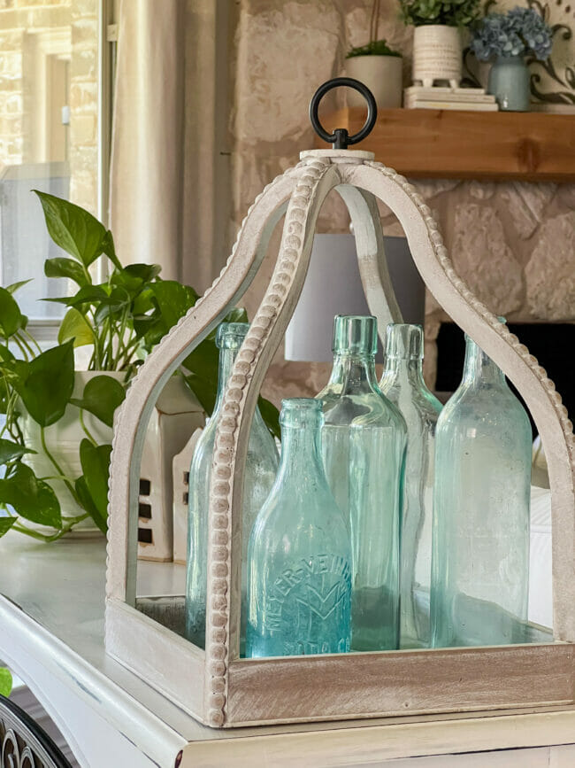 Blue bottles inside a white beaded lantern and plant in background