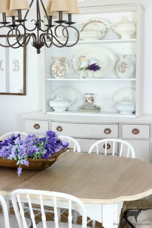 white hutch with china and purple flowers on table