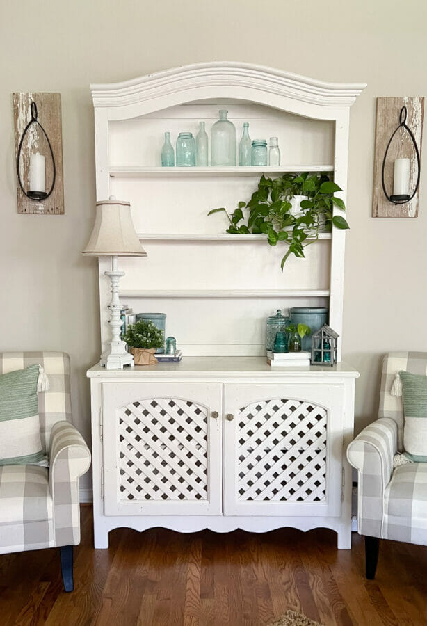 white hutch with plant, lamp, accessories and wall sconces