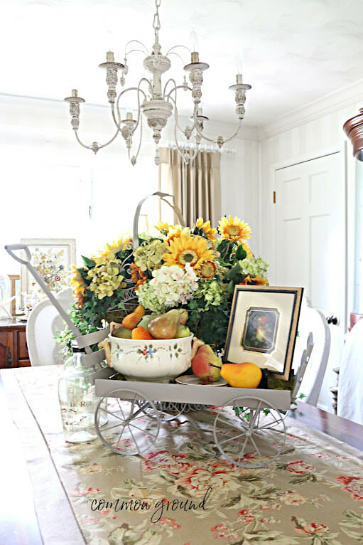 wagon on a table with flowers, fruits and framed photo of fruit