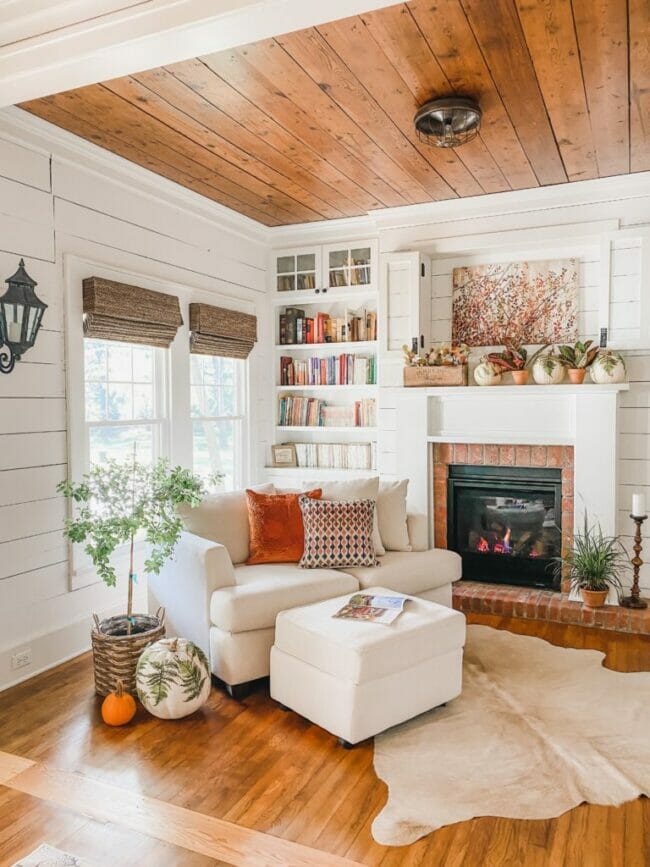 corner of room with white chair, mantel, bookshelf and fall decor