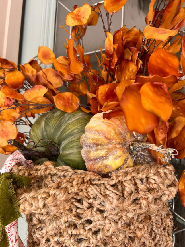 close up of orange fall stems and god and green pumpkins in basket