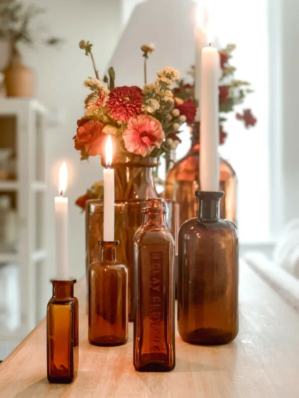 several brown bottles on table with white candles or fall flowers