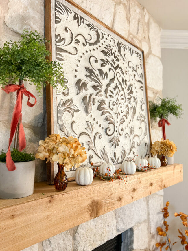 wood mantel with large damask artwork, topiaries and fall flowers