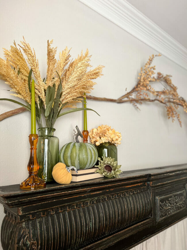 green fall vignette with pumpkins, vases and stems on black mantel