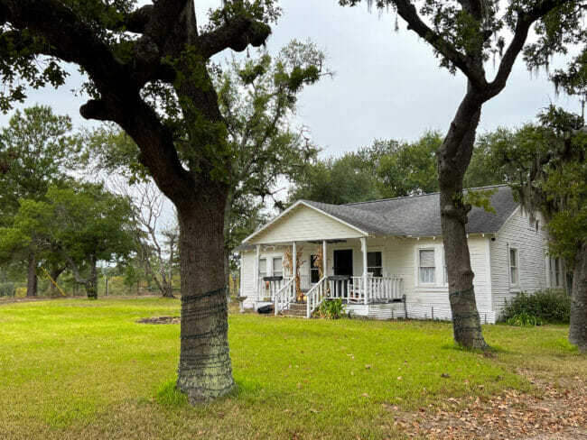 old white farmhouse with trees in front yard