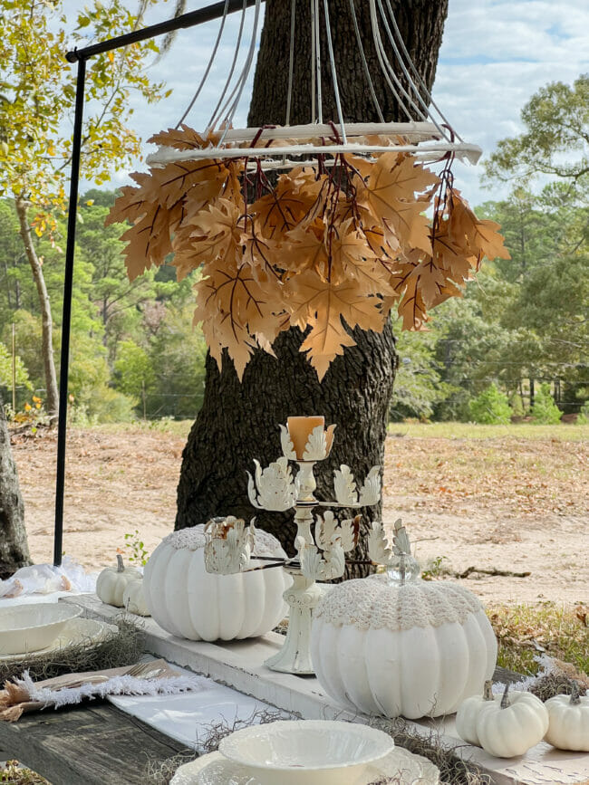 outdoor table with white pumpkins, fall leaves and white dishes