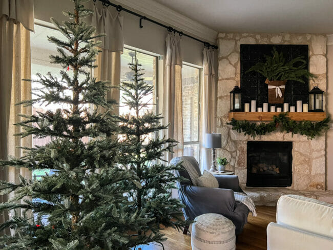 two natural Christmas trees with gray chair and stone fireplace with garland