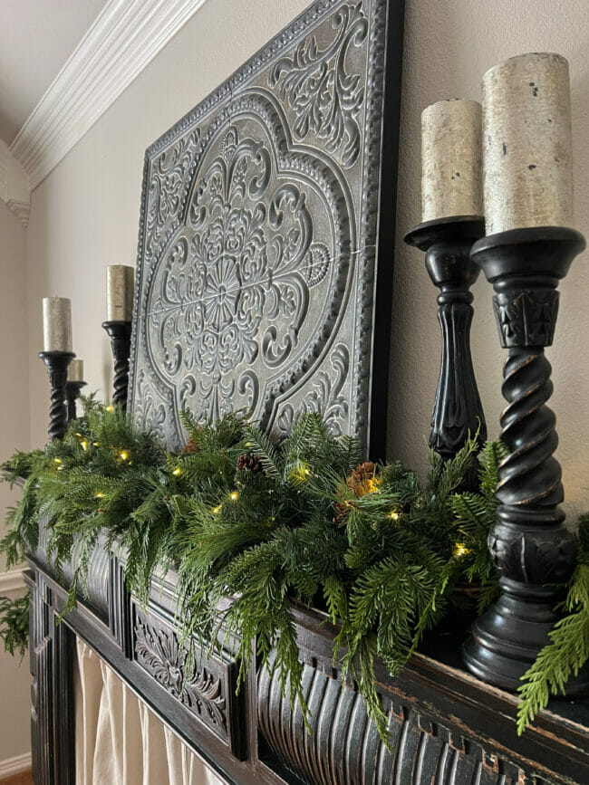 black mantel with black candlesticks, silver candles and double green garland with lights