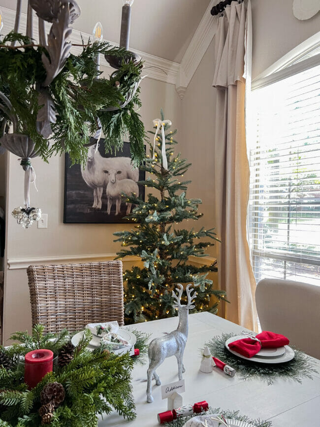 Christmas dining room with tree in corner, lamb print on wall and chandelier with ornaments