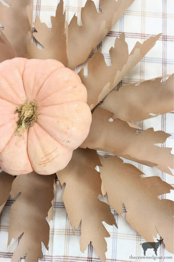 brown paper bag leaves sitting under a peach colored pumpkin