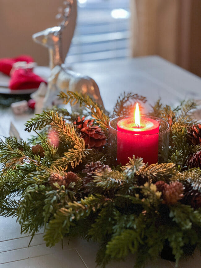 red candle centerpiece with a ring of greenery and pinecones