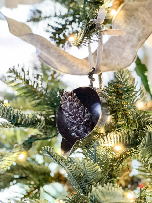 silver creamer with pinecone sitting inside and hanging on tree