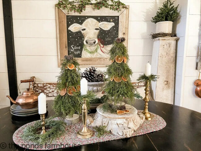 real greenery and oranges topiaries on table with candles and cow print on wall