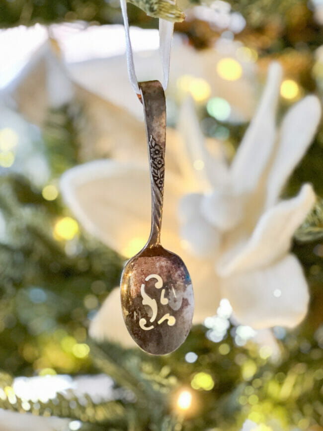 slotted silver spoon hanging on Christmas tree with white felt poinsettia in background