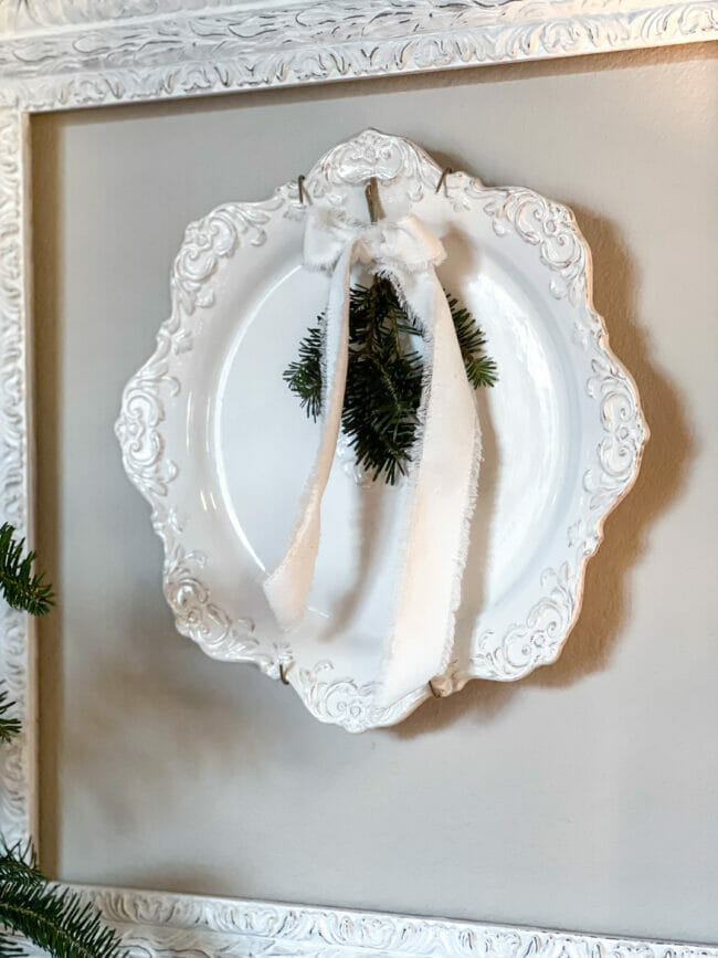 white plate hanging inside white frame with white bow and greenery