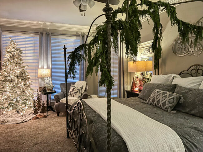 full Christmas bedroom with green garland, tree and gray chair with lamps